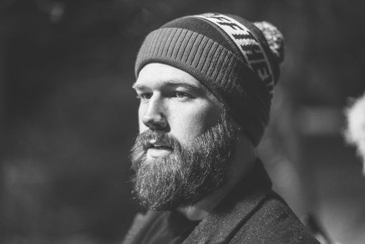 Bearded man in a knit beanie and coat gazing to the side in a black-and-white portrait