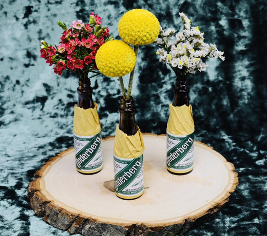 Front view of three Underberg herbal bitters bottles topped with colorful flowers on a natural wood slice