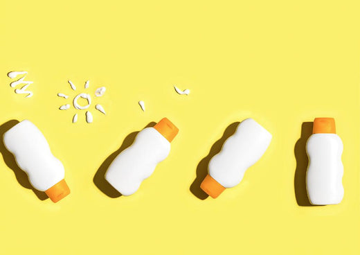 Overhead view of four white sunscreen bottles with orange caps on a bright yellow background