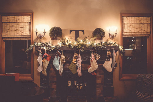 Christmas stockings hanging from a garland-decorated fireplace mantel in a warmly lit room