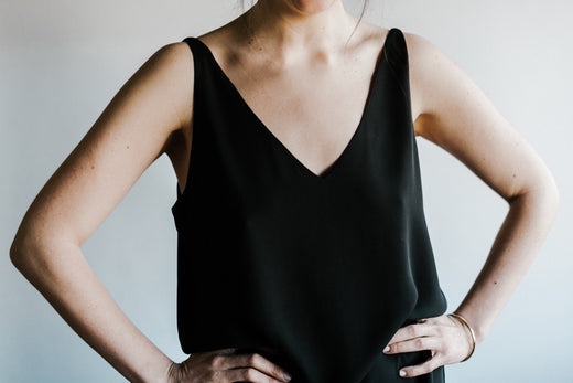 Woman in a black sleeveless top standing with hands on hips against a light background