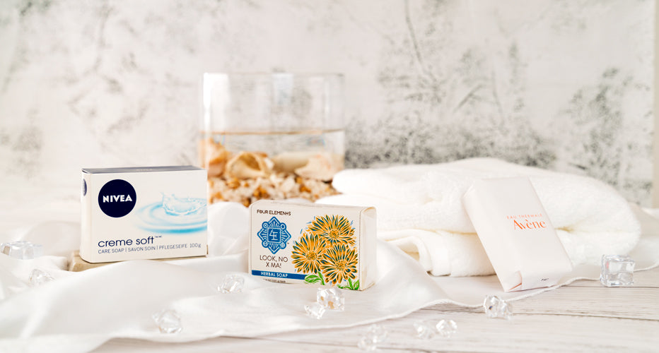 Assorted bar soaps displayed on white towels beside a glass of water and decorative stones