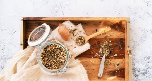 Dried herbs in an open jar with spoons on a wooden tray