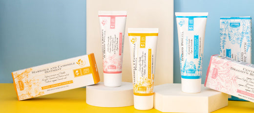 Natural ointment products displayed on geometric blocks against a colorful background