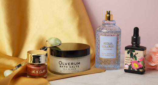 Mother’s Day bath and beauty gift selection arranged on a gold backdrop with bath salts, perfume, and a dropper bottle
