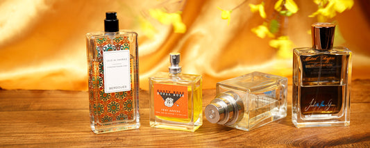 Fragrance bottles displayed on a wooden table with yellow flowers and warm fabric in the background