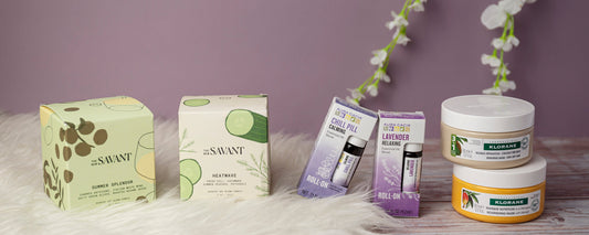 Staycation wellness products arranged on a white faux-fur rug and wooden table against a mauve background