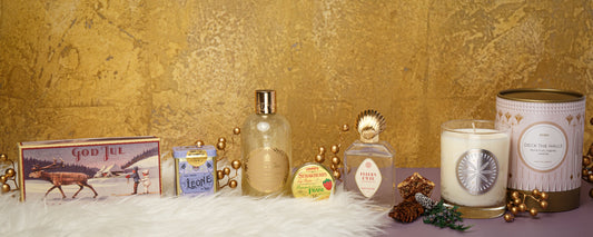 Vintage-inspired gifts arranged on faux fur with candles, fragrances, bath products, and holiday decor against a gold backdrop