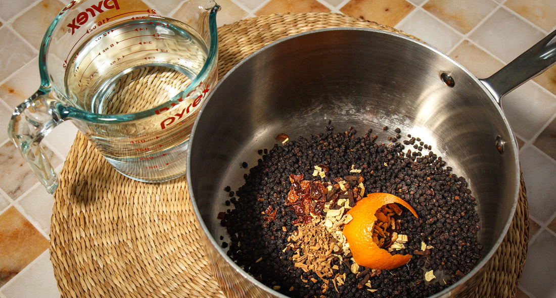 Saucepan of elderberries, orange peel, and spices beside a measuring cup for homemade elderberry syrup