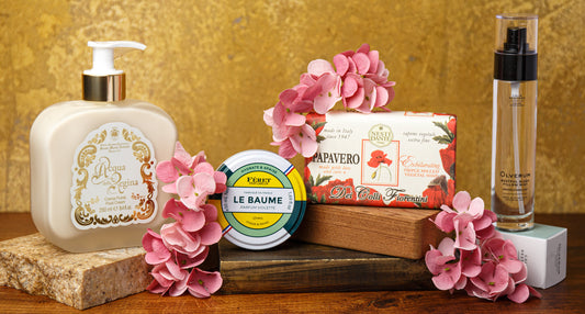 European beauty products arranged with pink flowers on stacked wooden boxes against a gold backdrop
