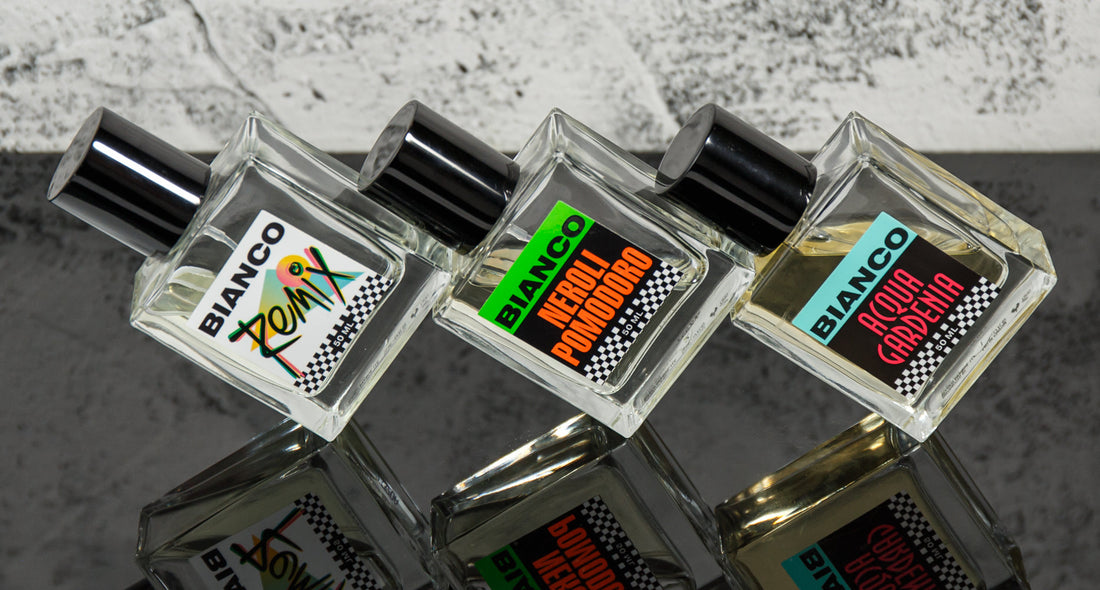 Overhead view of three Bianco Profumo fragrance bottles labeled ZUM, Neroli Pomodoro, and Acqua Gardenia on a reflective surface
