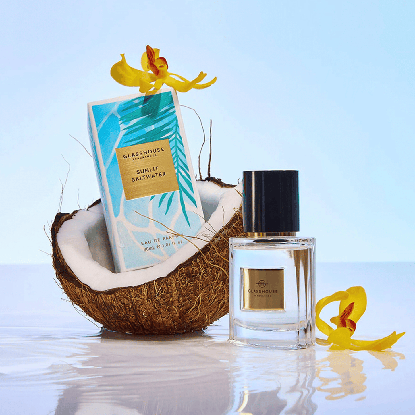 Alternate image of GlassHouse Sunlit Saltwater EDP bottle and packaging in a coconut shell along with tropical flowers 