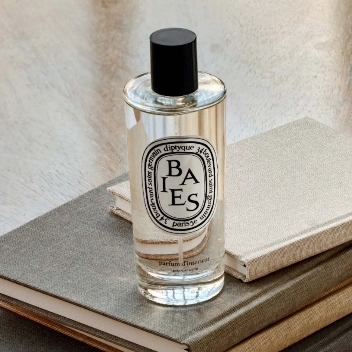 Front view of Baies Room Spray showcasing a clear bottle with black cap on stacked books