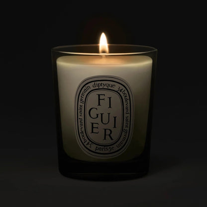 Front view of Figuier Fig Tree Small Candle showcasing its lit wick and cream label in a dark glass jar