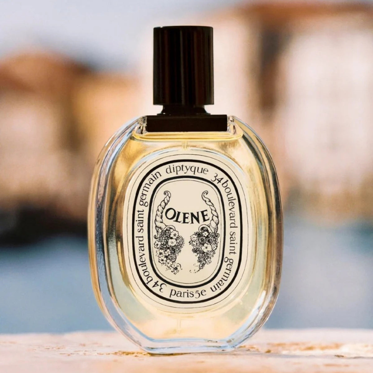Front view of diptyque Paris Olene Eau de Toilette showcasing clear bottle and black cap against blurred background