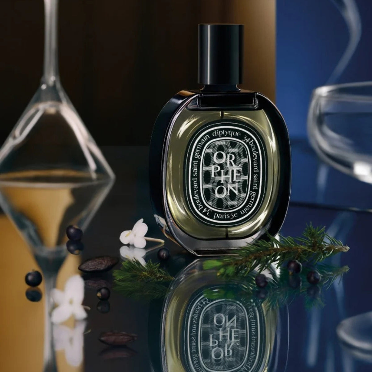 Front view of diptyque Paris Orpheon Eau De Parfum showing its oval black bottle and cap with flowers and evergreen branches